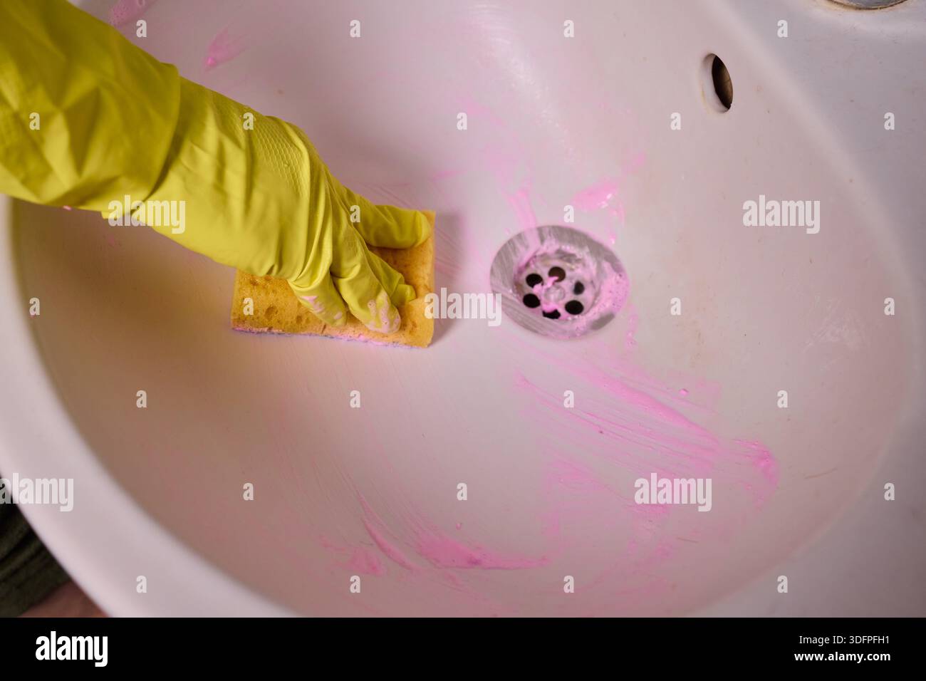 Propriétaire prépare la baignoire soigneusement, gros plan de l'écume de savon de nettoyage des mains du drain de la baignoire, vue détaillée de la personne désinfectant la baignoire avec de la mousse rose Banque D'Images