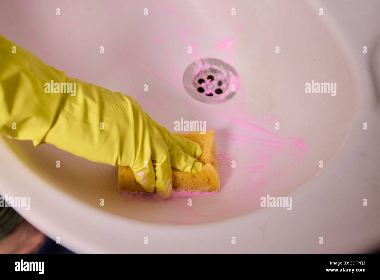 Propriétaire prépare la baignoire soigneusement, gros plan de l'écume de savon de nettoyage des mains du drain de la baignoire, vue détaillée de la personne désinfectant la baignoire avec de la mousse rose Banque D'Images