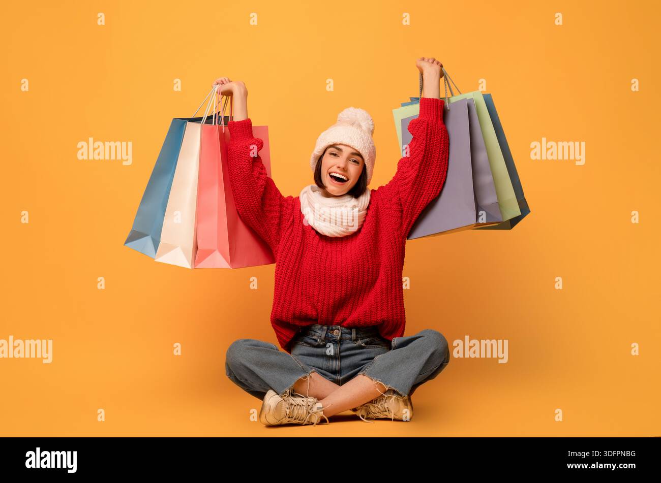 Ventes saisonnières. Femme heureuse tient des sacs à provisions, assis sur fond jaune et souriant à la caméra Banque D'Images