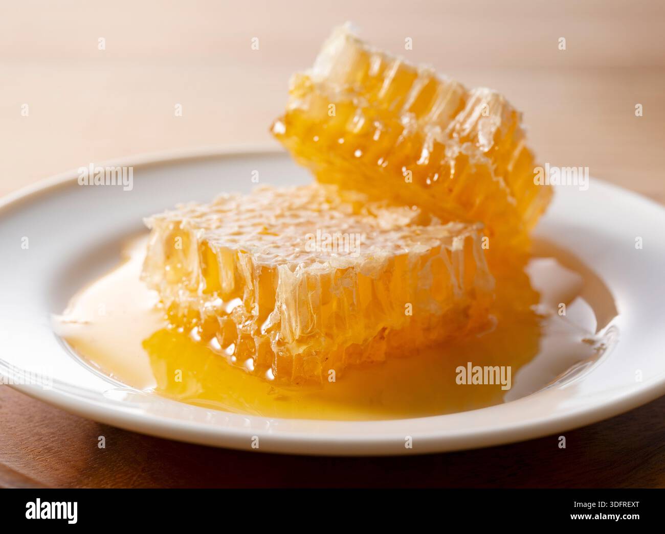 Nid d'abeilles crues fraîches sur plaque blanche avec du miel qui goutte à goutte Banque D'Images