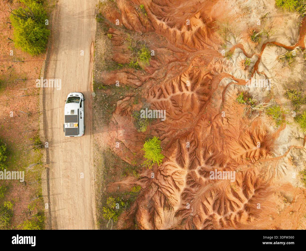 Vue aérienne d'un van blanc solitaire s'aventure le long d'une route poussiéreuse, contrastant avec les motifs complexes de la terre rouge vibrante, Huila, Huila, Colombie. Banque D'Images