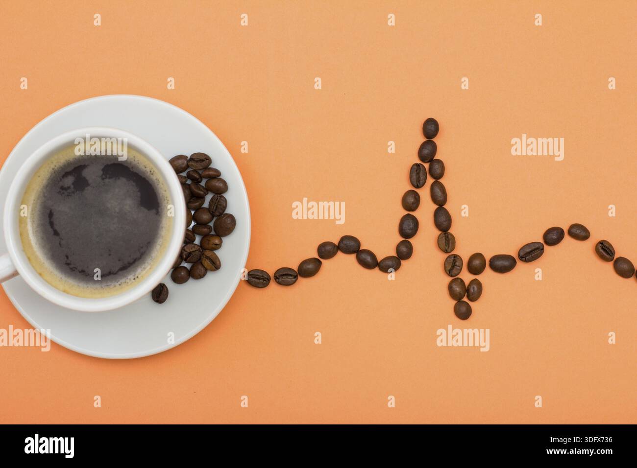 Tasse de café en porcelaine blanche sur les grains de café avec soucoupe pliée dans la forme d'un cardiogramme sur fond de couleur pêche. Vue d'en haut Banque D'Images