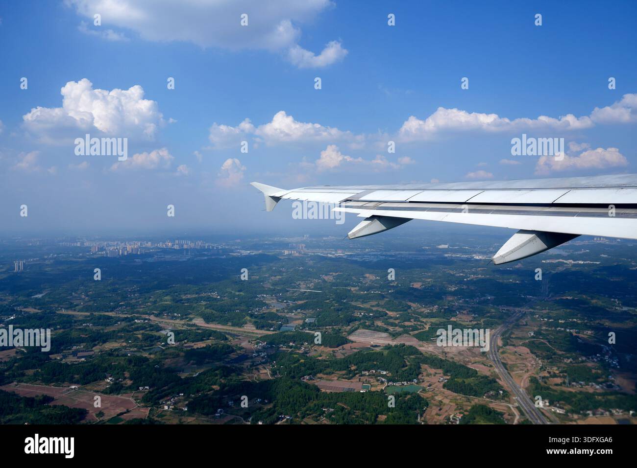 Aile d'avion, hublot, vue d'avion sur aile. L'avion survole une ville avec un champ vert en dessous Banque D'Images