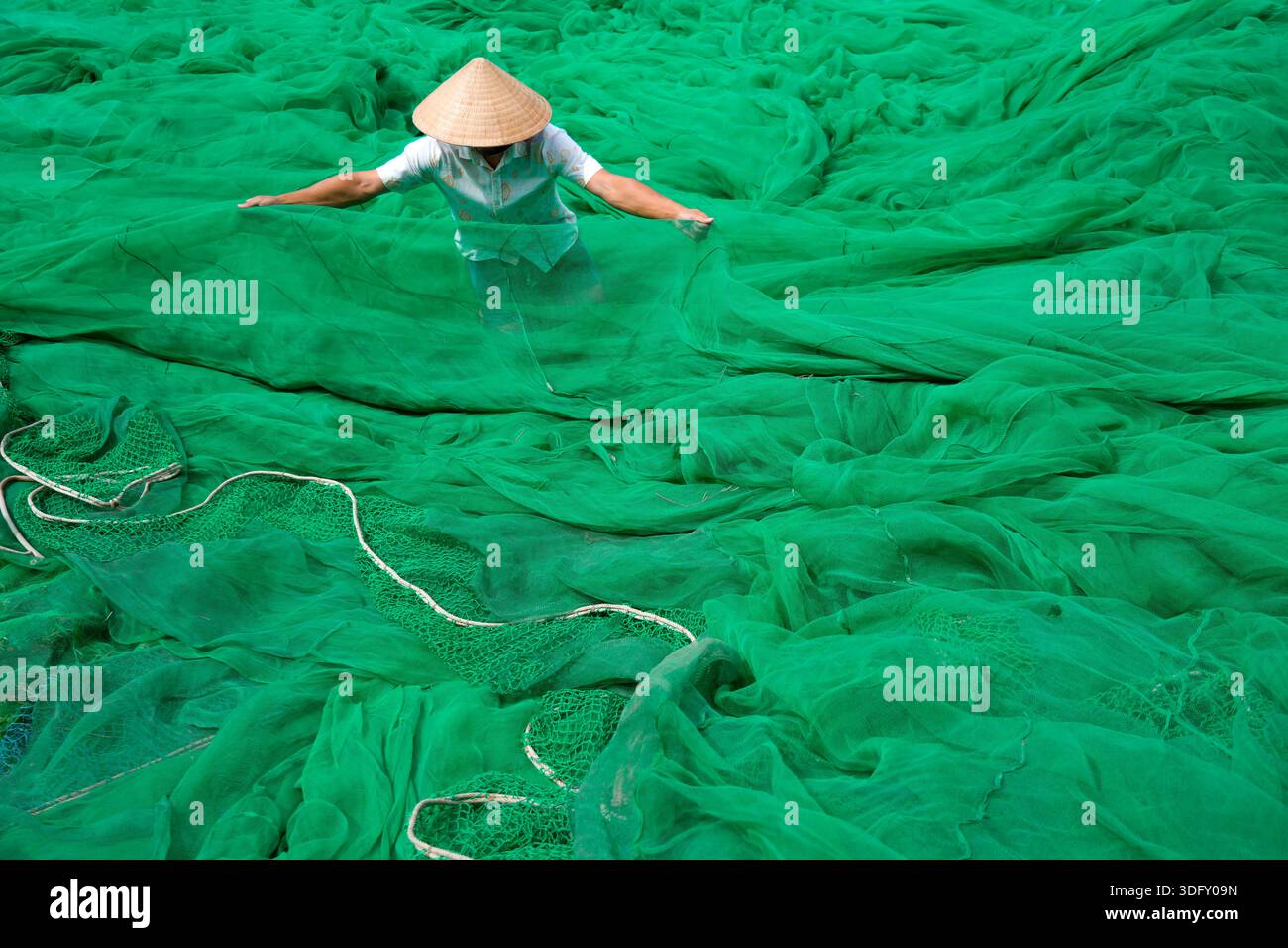 Homme Guy étendant ses bras large dans le chapeau authentique traditionnel vietnamien démêler les filets de pêche verts se préparant à la pêche et à sortir en mer. Banque D'Images