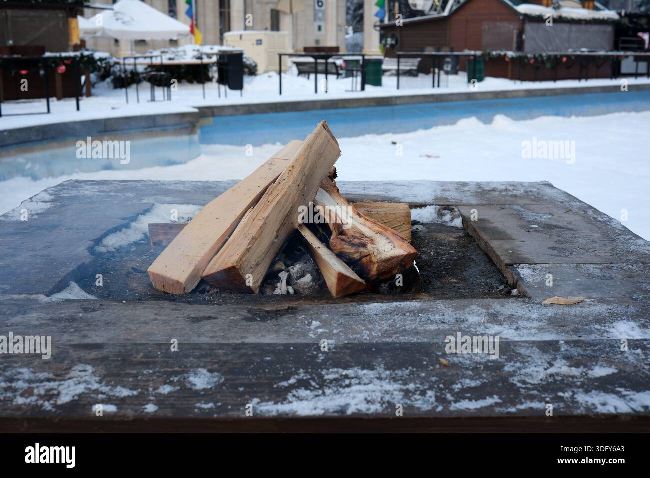 Des flammes chaudes dansent au sommet des rondins dans un foyer tandis que la neige couvre le village. Banque D'Images