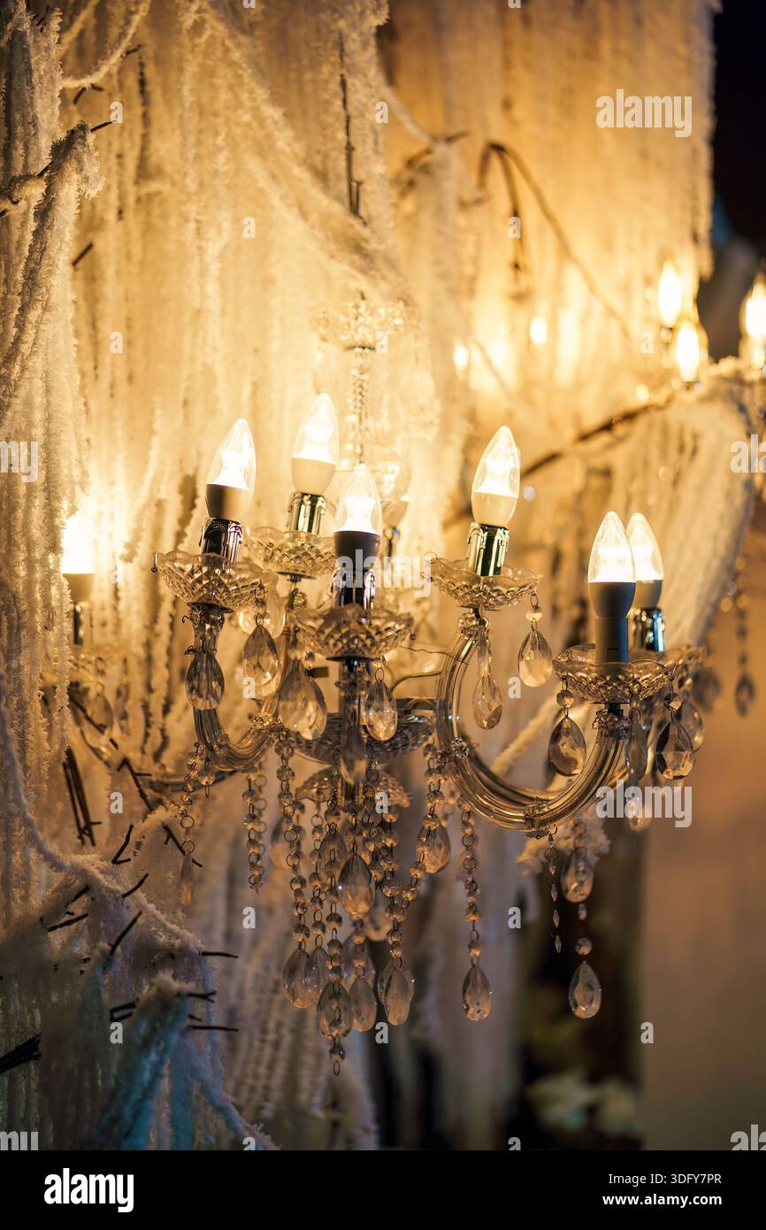 Gros plan lustre en cristal orné illuminé avec des ampoules blanches chaudes entourées d'une décoration florale blanche suspendue, créant pour le festival de mariage Banque D'Images