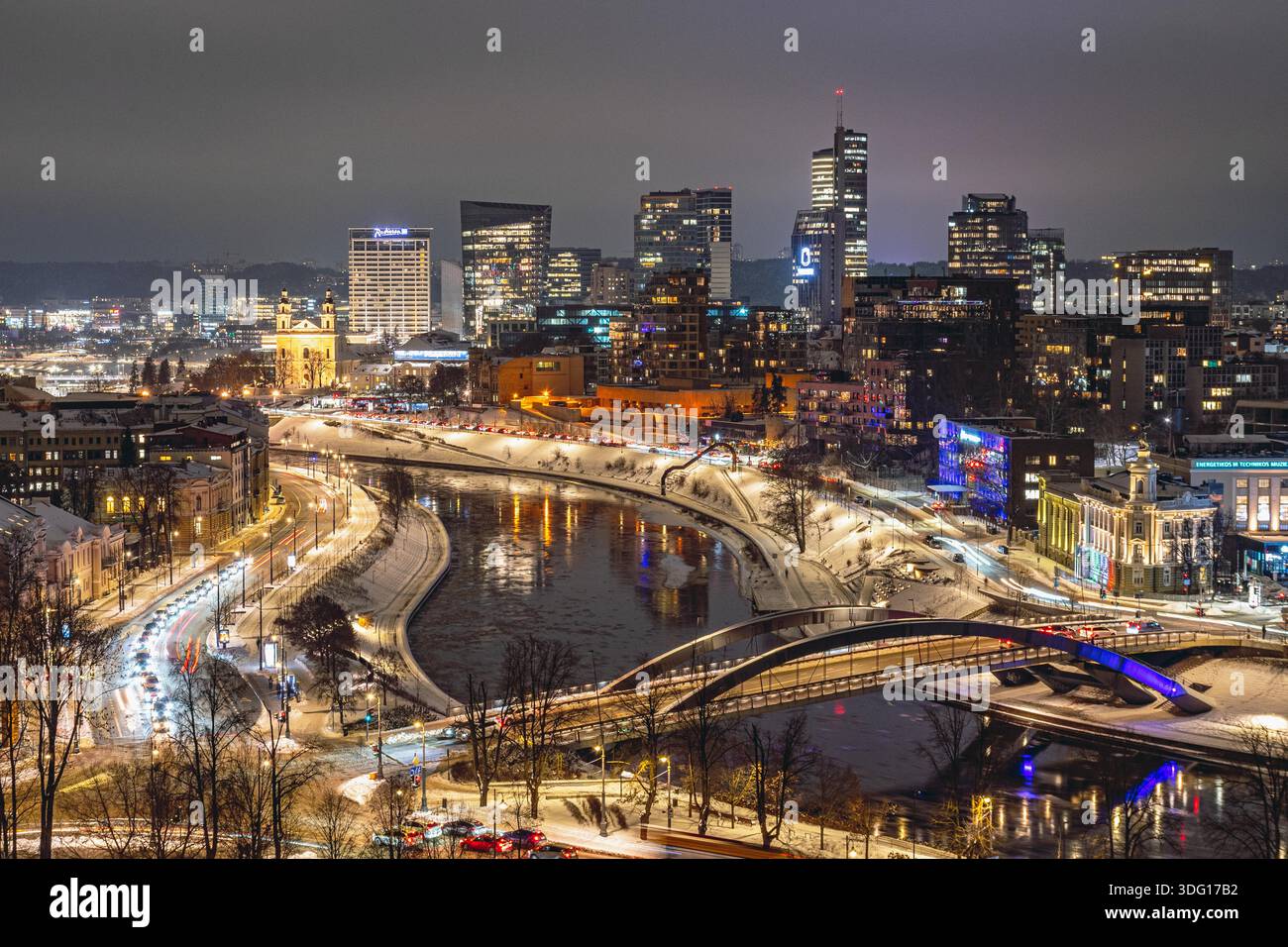 Une vue nocturne hivernale de Vilnius montrant un paysage urbain lumineux le long de la rivière Neris, avec des ponts illuminés, un trafic fluide Banque D'Images