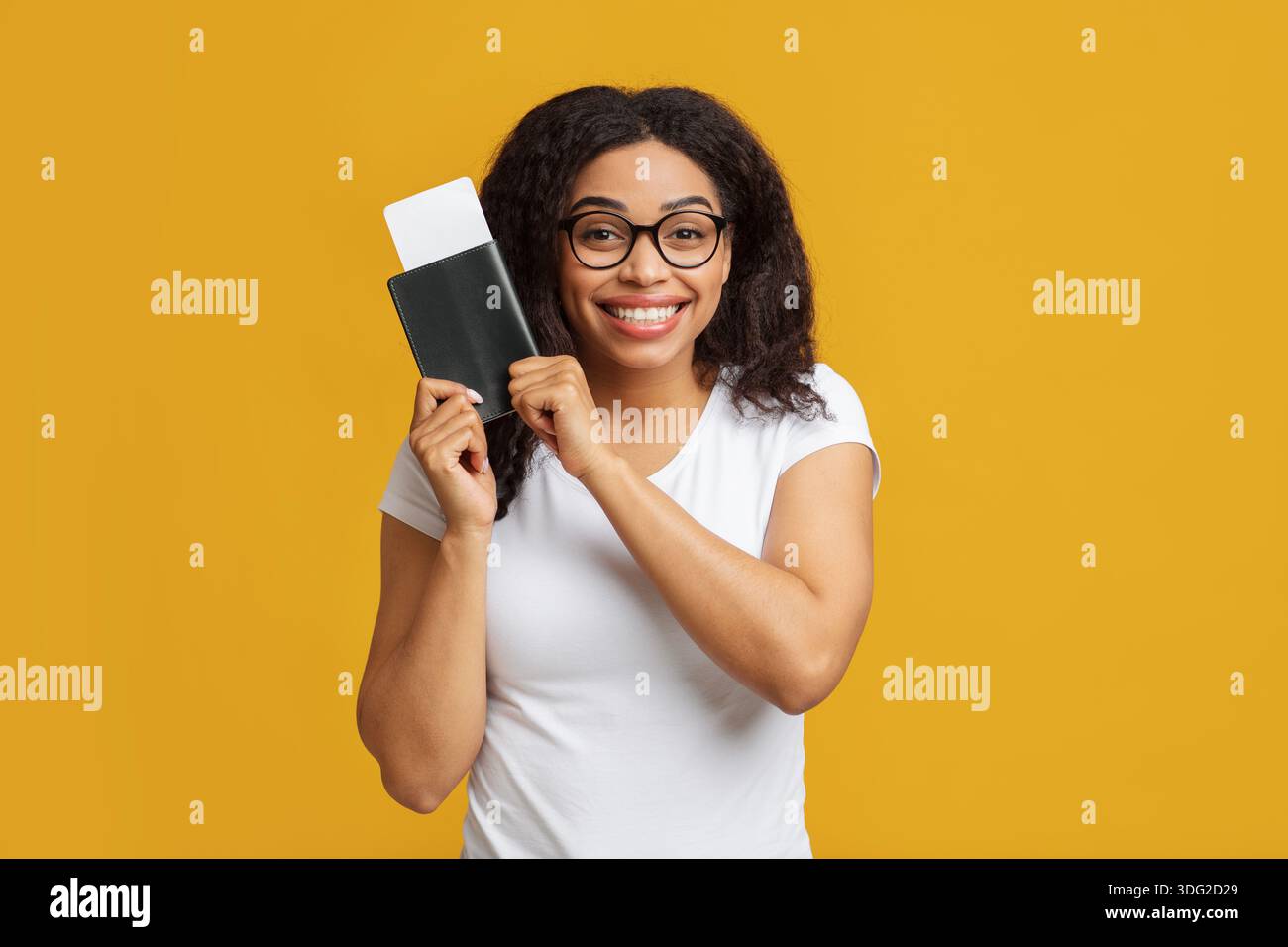 Touriste afro-américaine excitée avec passeport et billets d'avion se préparant pour les vacances, fond jaune Banque D'Images