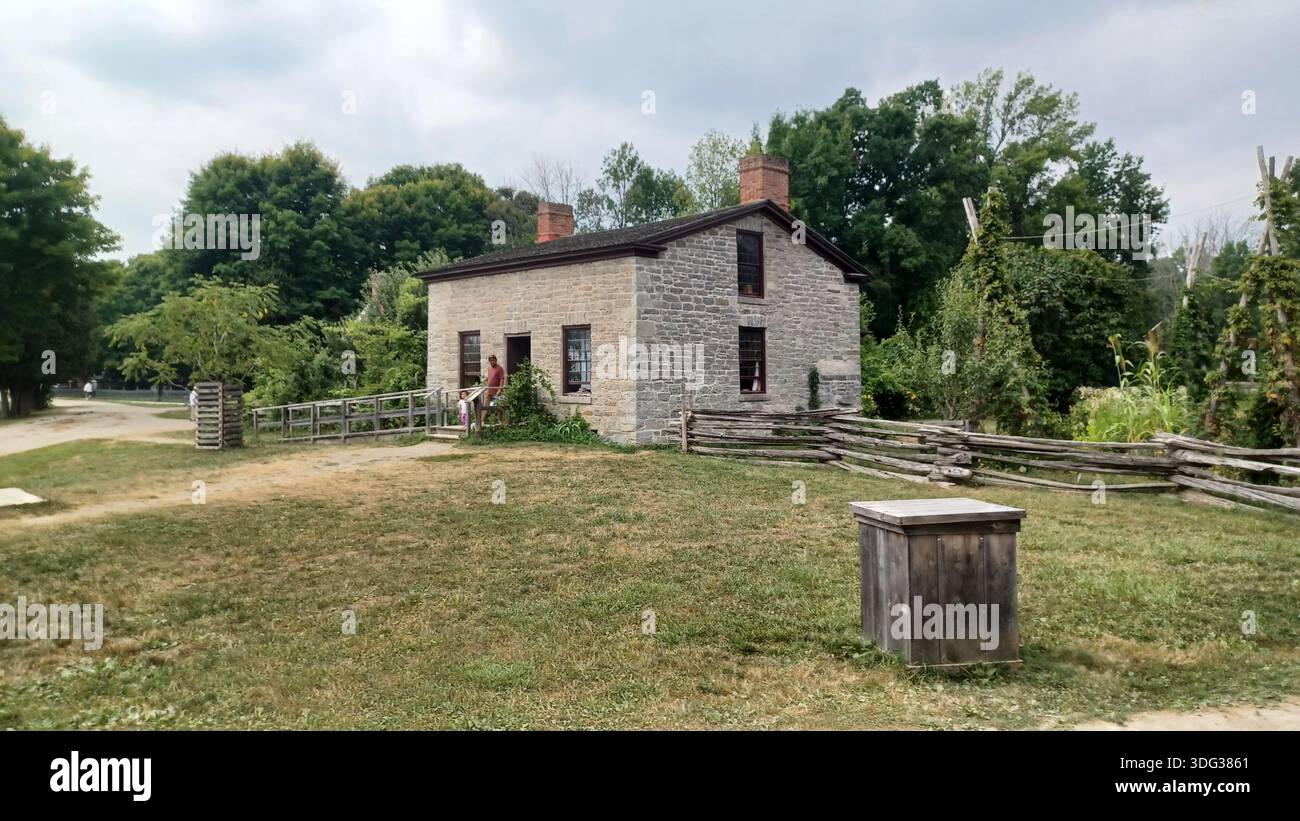 Morrisburg, ON, Canada - 3 août 2025 : Upper Canada Village mettant en vedette une maison historique en calcaire avec une clôture en rail fendu, préservant le XIXe siècle l Banque D'Images
