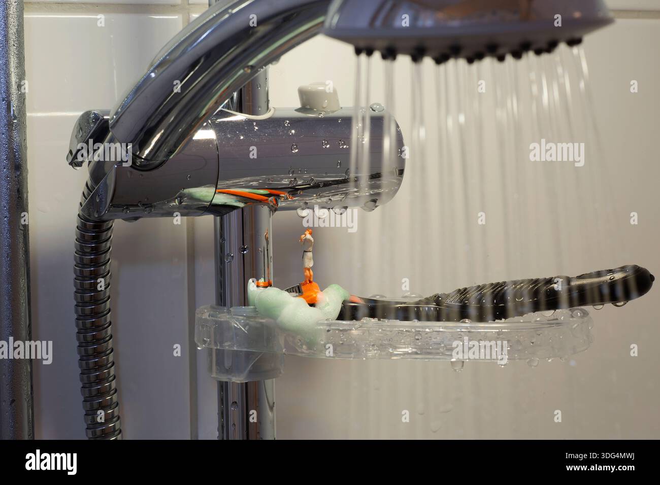 Figurine miniature gros plan d'une douche de salle de bains avec de l'eau courante tombant sur un rasoir placé sur une étagère de douche. Banque D'Images
