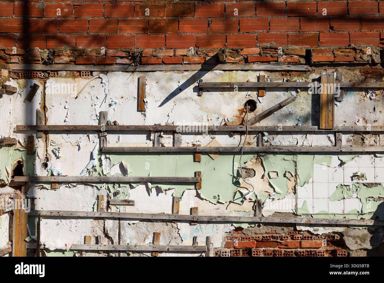 Un mur de bâtiment détérioré avec des briques rouges apparentes, du plâtre pelable, des restes de vieille peinture et une ossature en bois. Banque D'Images