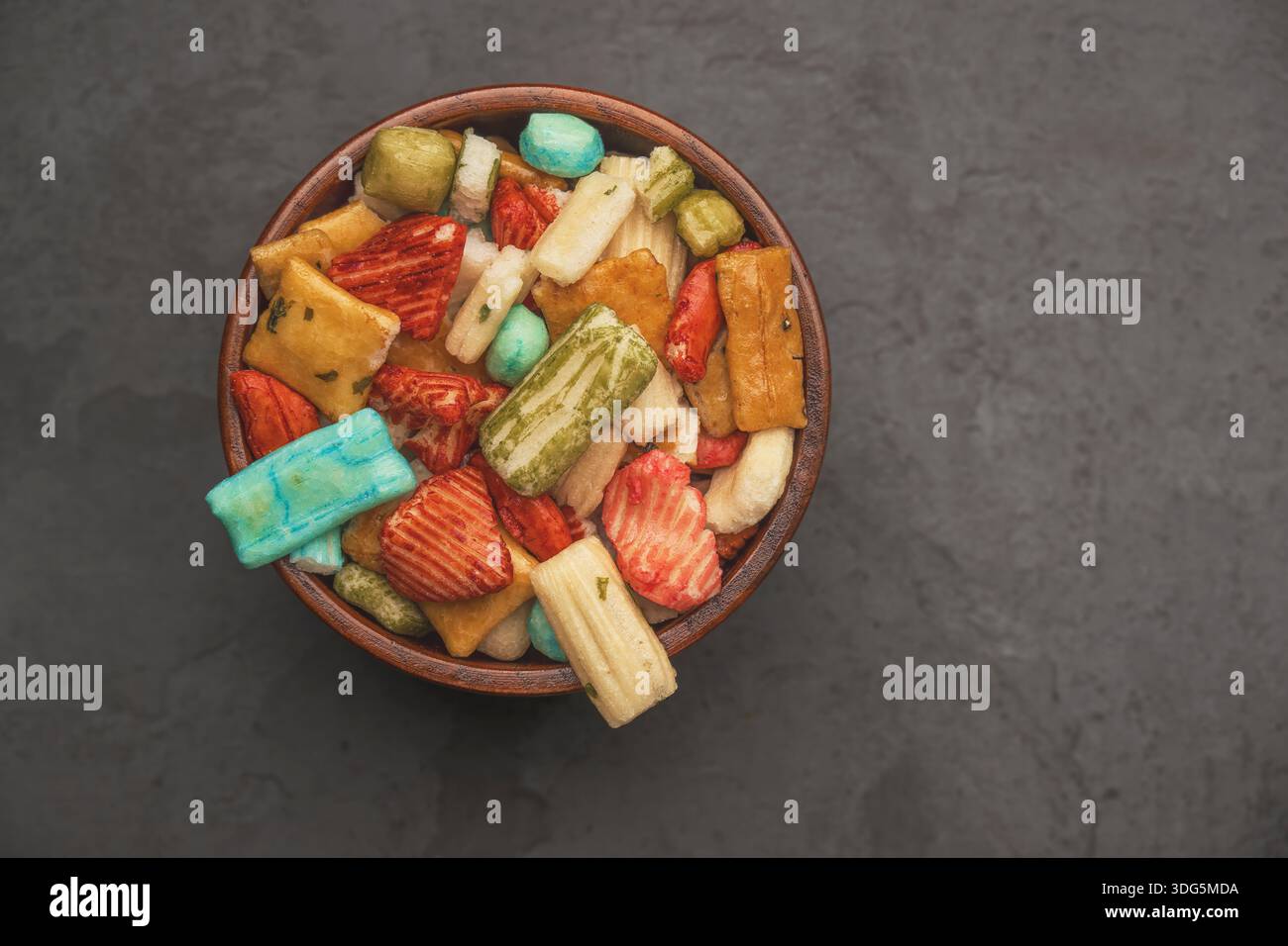 Gros plan de craquelins de riz japonais dans un bol avec fond isolé. Craquelins de riz colorés assortis sur fond noir. Collations de fête. Banque D'Images