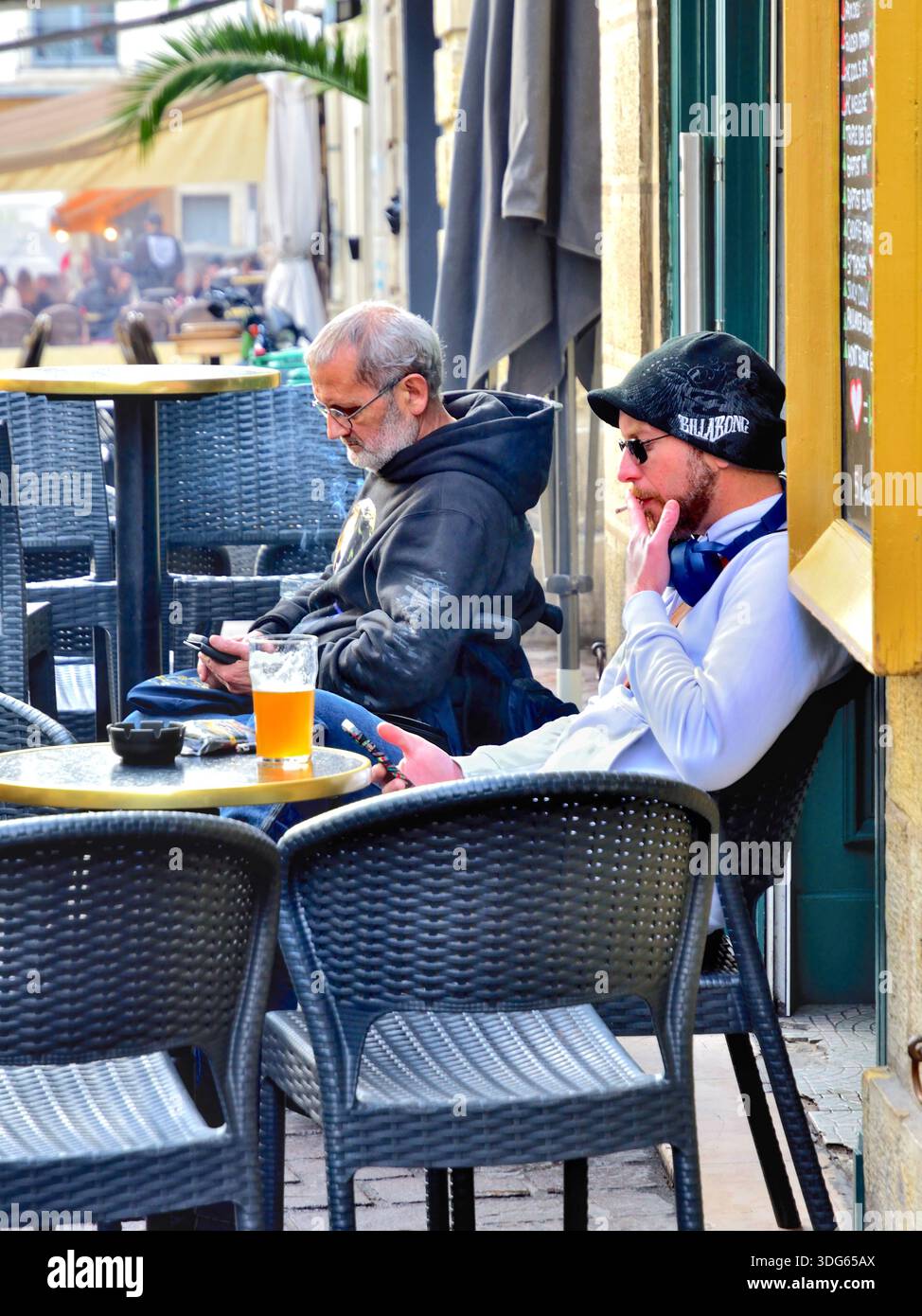 Deux hommes individuels concernant leurs smartphones sur une terrasse de café en plein air - Tours, Indre-et-Loire (37), France. Banque D'Images