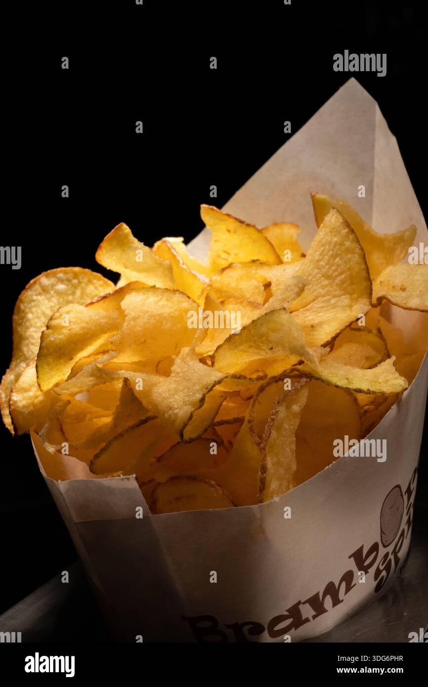 Frites croustillantes dorées servies dans un cône de papier sur un fond sombre, en-cas de restauration rapide avec éclairage studio spectaculaire et espace de copie. Banque D'Images