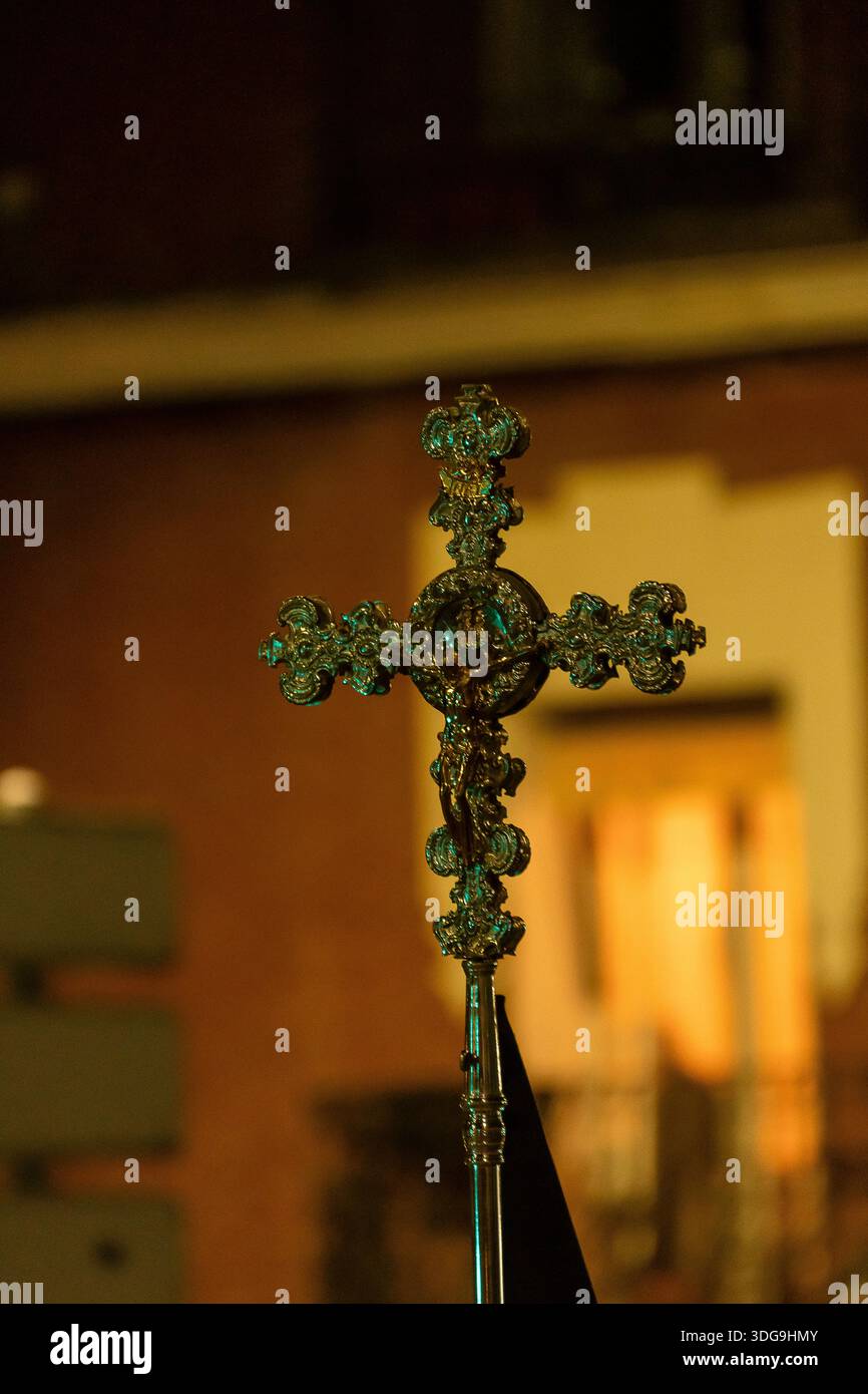 Une croix magnifiquement travaillée se détache sous un éclairage tamisé lors d'une procession religieuse nocturne dans une ville. Banque D'Images