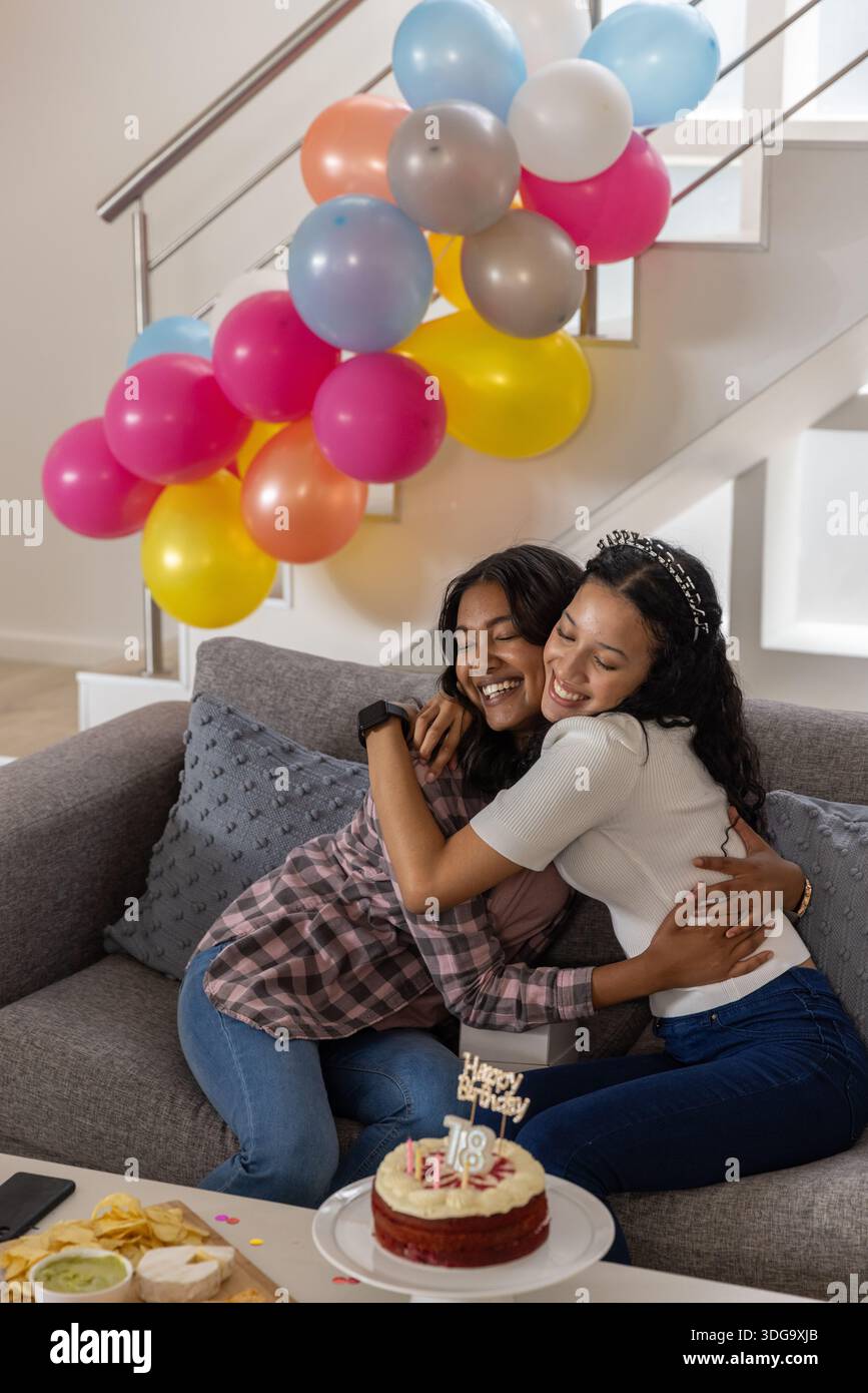 Maman et fille diversifiées dans le salon célébrant l'anniversaire avec gâteau, ballons et Banque D'Images
