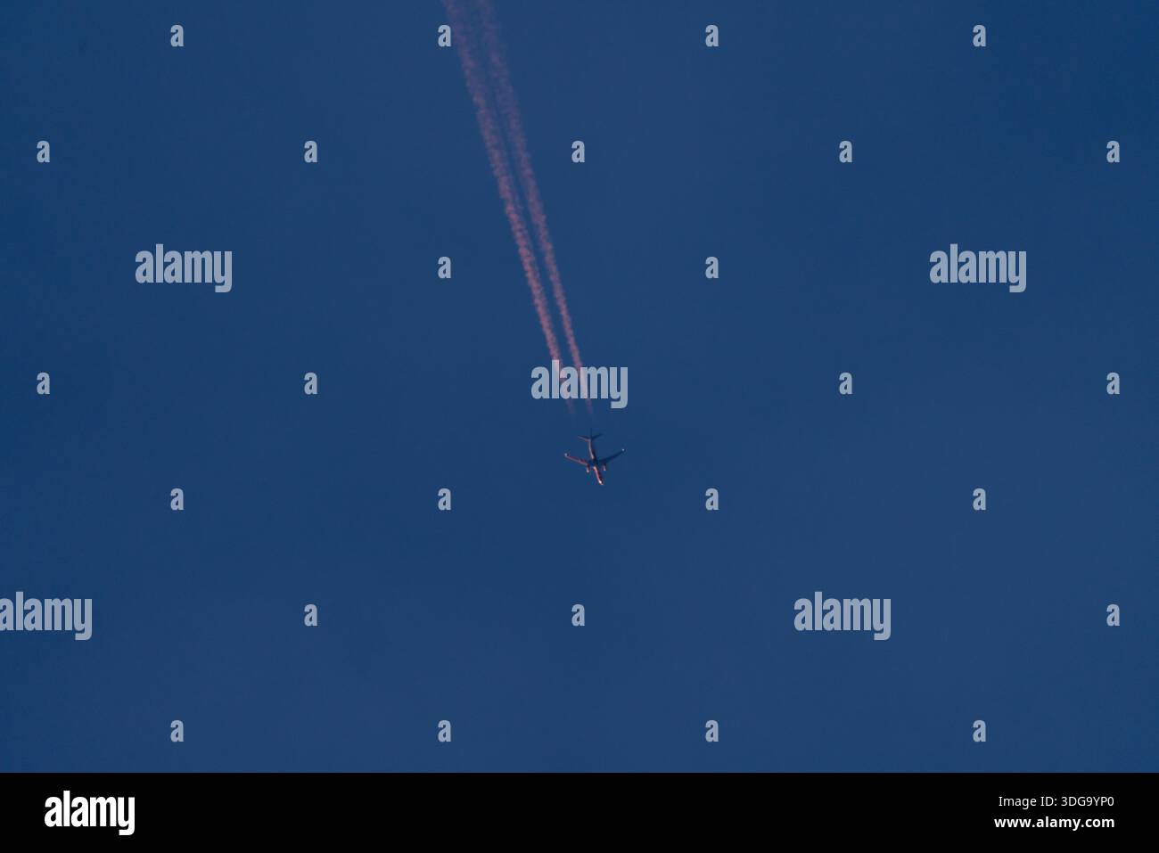 Avion volant haut créant des traînées à travers le ciel bleu profond Banque D'Images