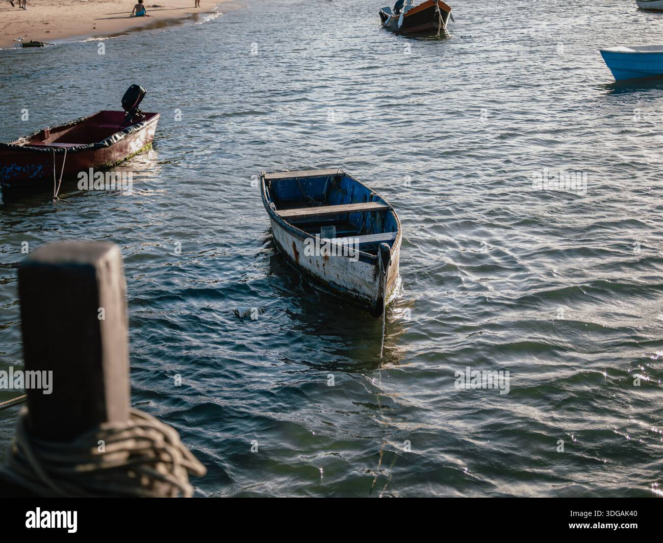 Petit bateau amarré dans l'eau côtière peu profonde près d'une plage par un jour couvert. Banque D'Images