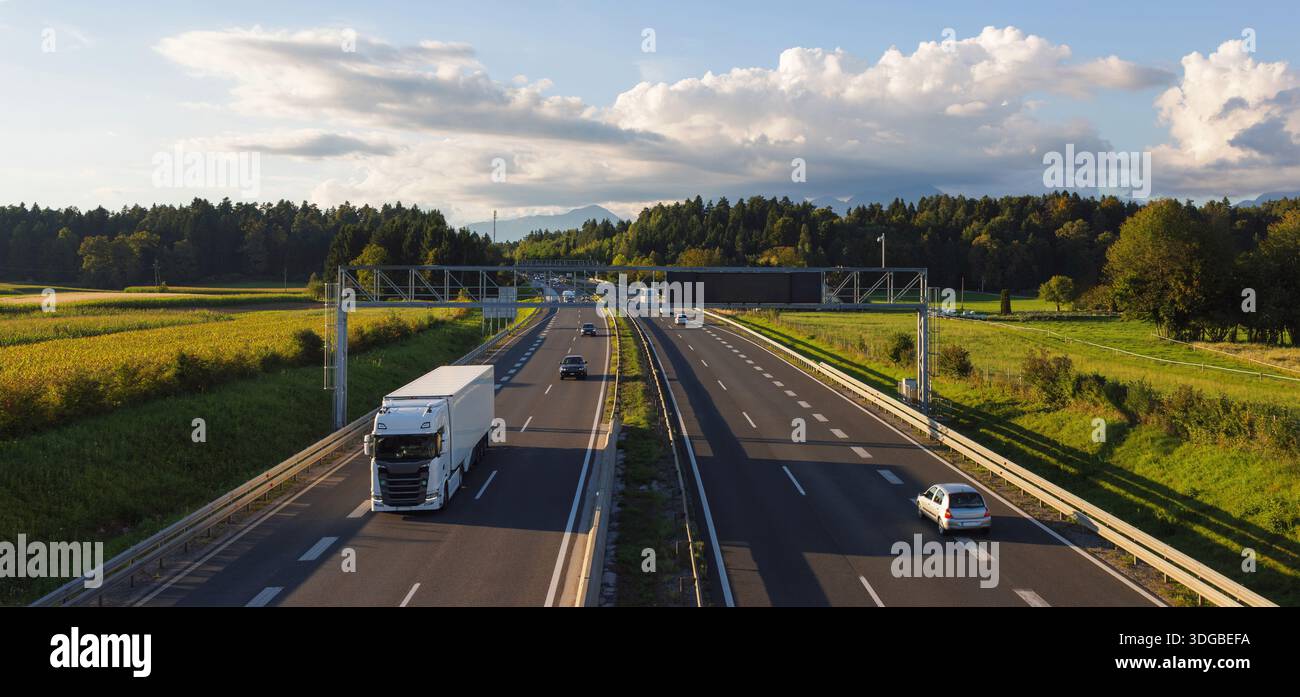Les camions circulent sur une autoroute entourée de champs, conduisant des marchandises pour le commerce électronique et soutenant les réseaux logistiques. Banque D'Images