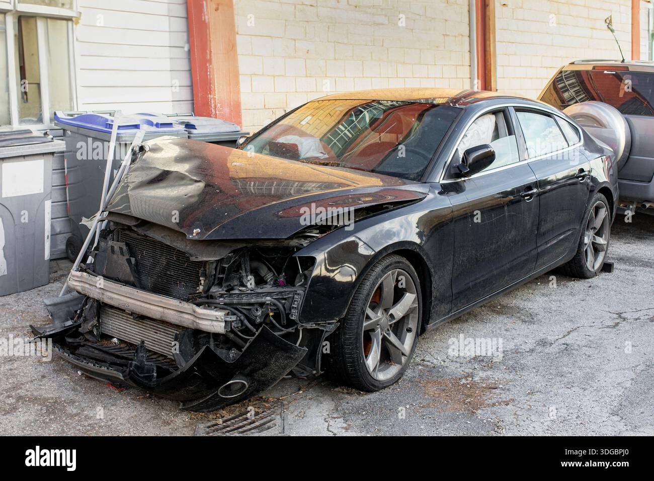 Voiture de luxe lourdement endommagée après un accident de la route, garée à l'extérieur en attente de réparation, avec impact visible à l'avant et dommages à la carrosserie Banque D'Images