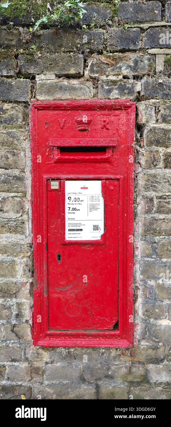 Vieille boîte aux lettres en métal rouge montée sur un mur de briques altérées. Évoquant l'histoire urbaine, le patrimoine de la communication et le passage du temps dans une ville : Londres - Image de stock capturée avec un smartphone