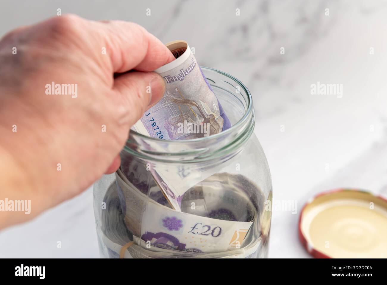 Un gros plan d'une personne économisant de l'argent en mettant des billets de banque Sterling Pound dans un bocal en verre. Banque D'Images