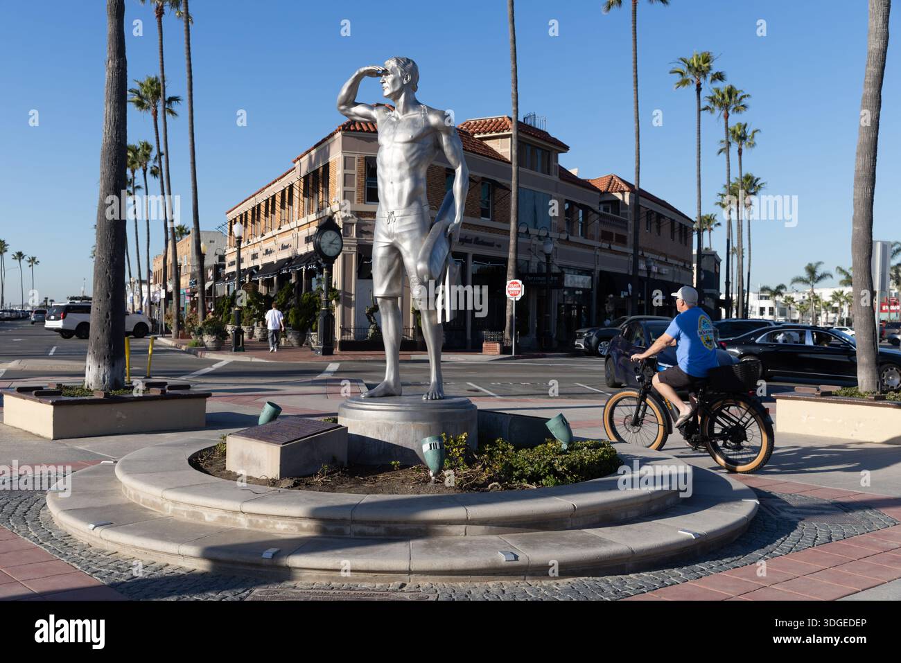 Statue de surfeur se dresse à une intersection de rue près de la jetée de Newport Beach alors qu'un cycliste passe par, Newport Beach, Californie. Banque D'Images