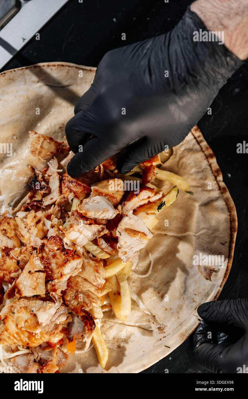 Le chef met du kebab à la viande. Un chef place la viande de kebab fraîchement cuite dans un shawarma ouvert pendant l'assemblage. Banque D'Images