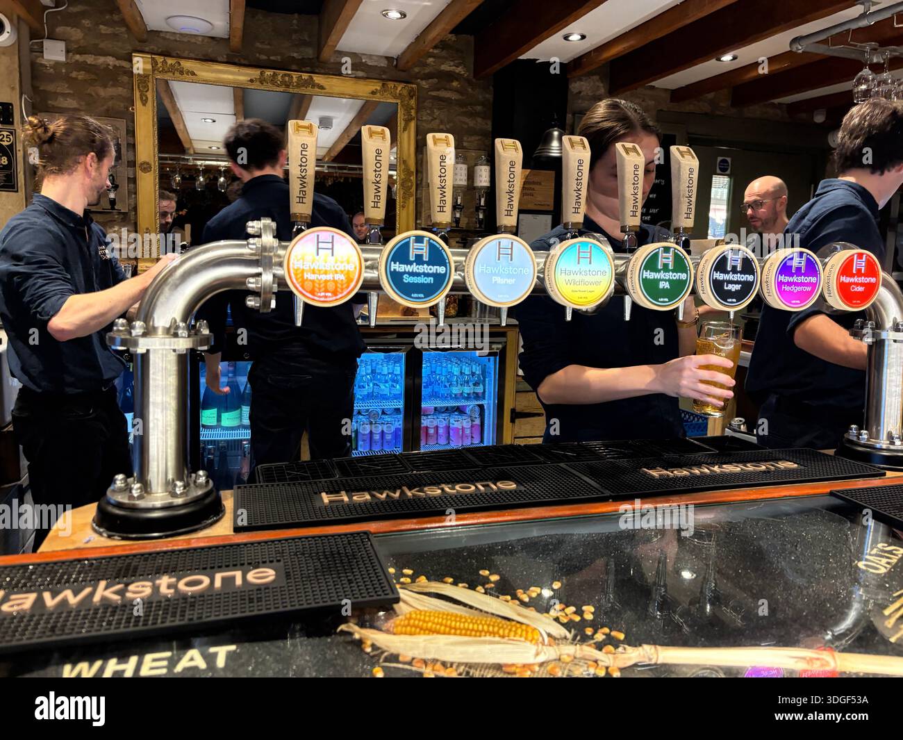 Barman versant de la bière pression fraîche des robinets à l'intérieur d'un pub de brasserie artisanale animé avec les clients et le personnel en arrière-plan. Banque D'Images