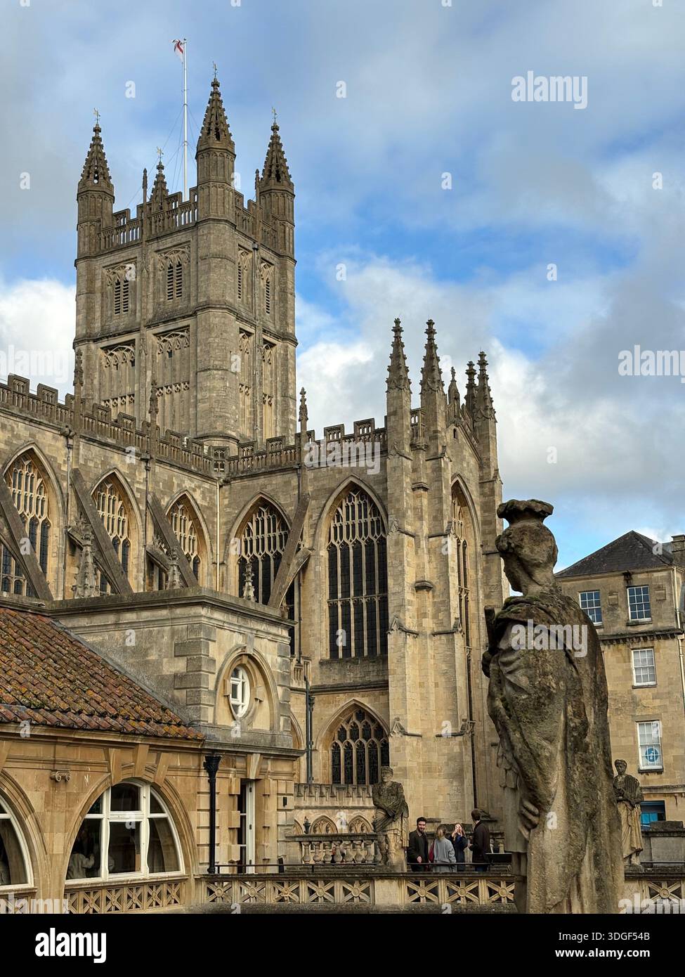 Statue historique en pierre surplombant le complexe des thermes romains avec l'abbaye de Bath en arrière-plan à Bath, en Angleterre, sous un ciel partiellement nuageux. - Image de stock capturée avec un smartphone