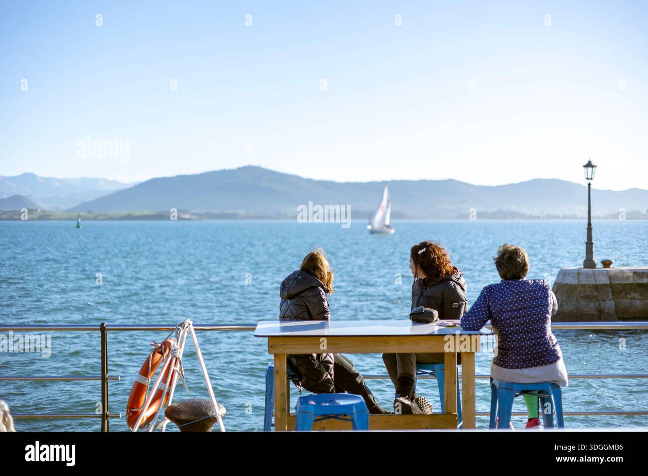 Santander, Espagne – 19 novembre 2021 : trois femmes s’assoient à une table sur la promenade du front de mer à Santander, regardant la baie avec des voiliers et des montagneuses Banque D'Images