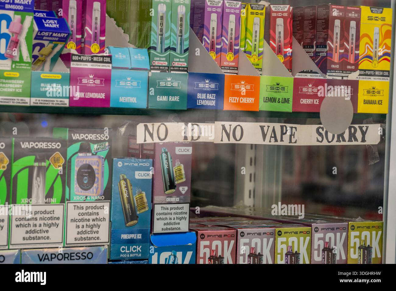 Sélection colorée de vapeurs aromatisées exposées dans une vitrine de magasin de vapotage de grande rue avec une pancarte « NO ID NO VAPE, SORRY » restrictions d'âge sur les vapeurs. Banque D'Images