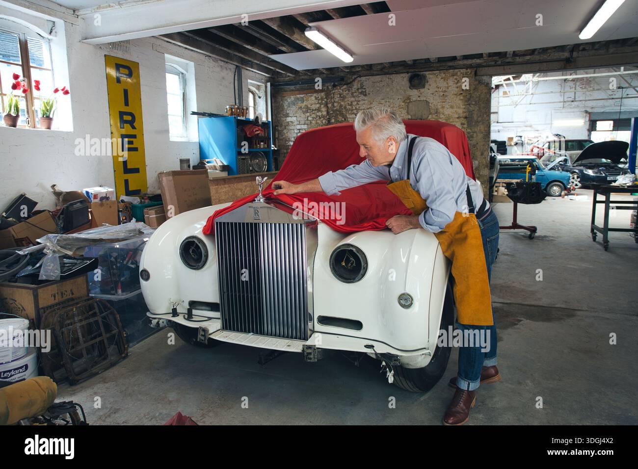 Un moment dramatique de dévoilement alors qu'une housse en tissu rouge est retirée pour révéler une Rolls-Royce classique entièrement restaurée. Banque D'Images