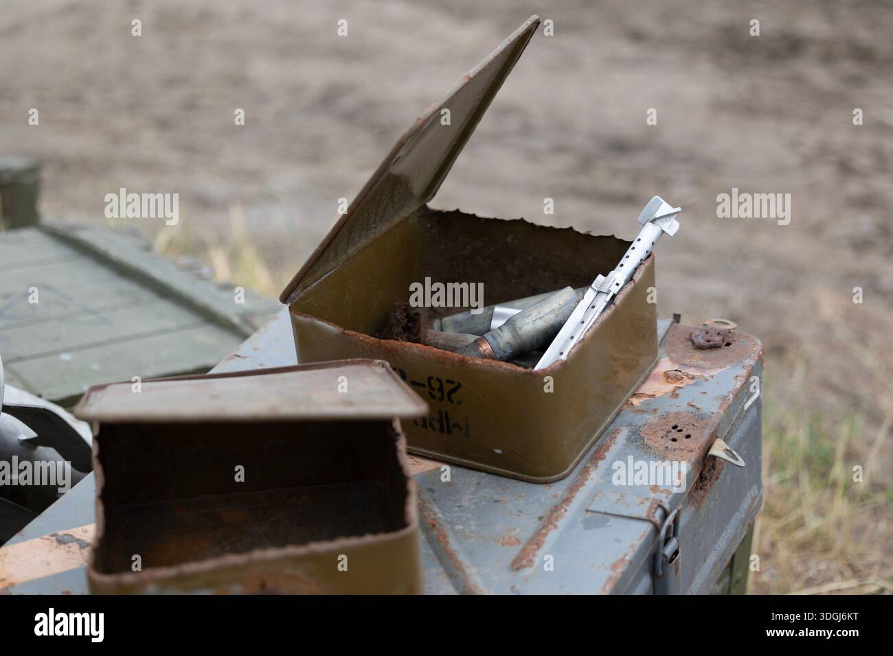 L'invention concerne une boîte de munitions rouillée ouverte remplie d'enveloppes usées, de maillons de courroie et d'un stabilisateur d'aileron arrière RPG-7. Jetés sur un champ de bataille, ces restes s Banque D'Images