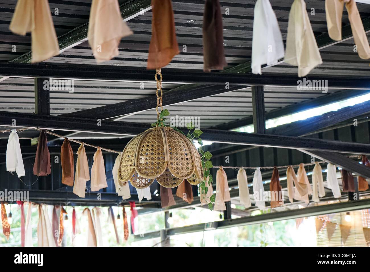 Lampe en rotin tissé avec bords festonnés suspendue dans un espace extérieur confortable décoré de vignes. Banque D'Images