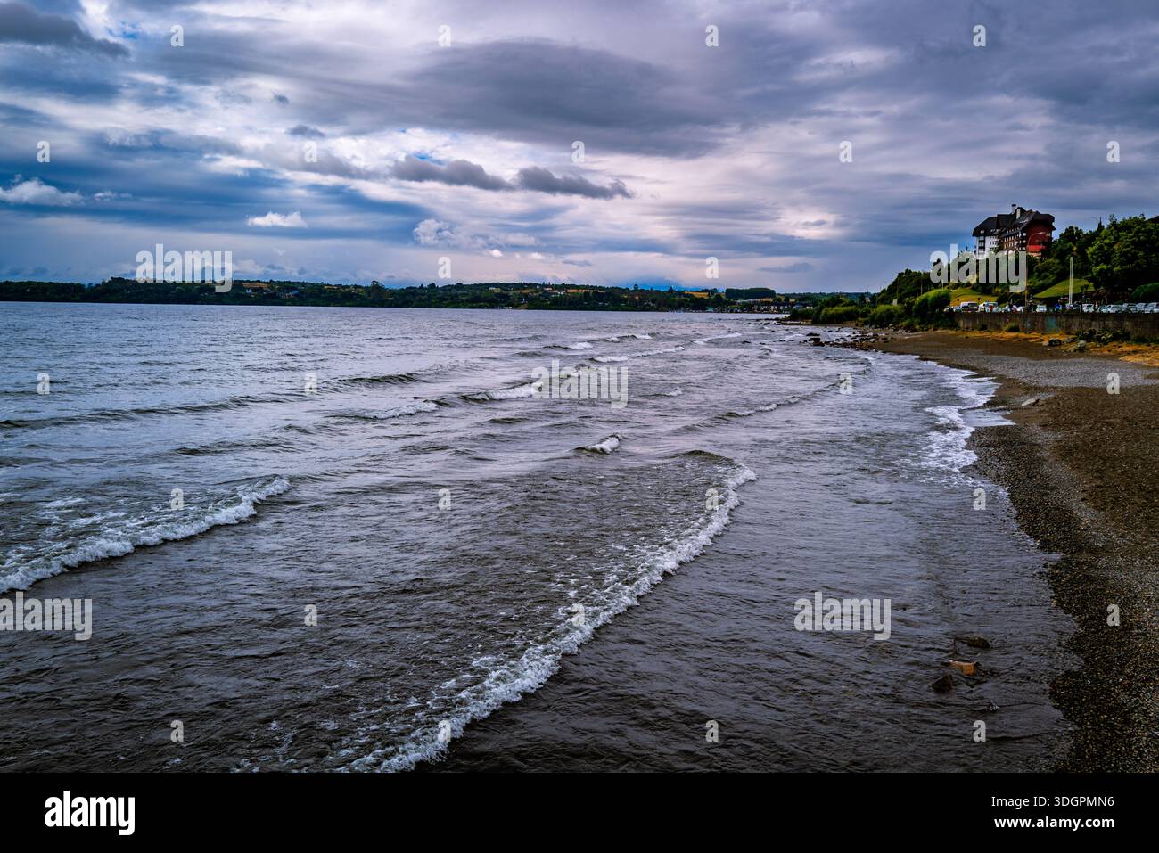 Un paysage sombre avec une eau agitée et un ciel spectaculaire avec un hôtel sur une colline lointaine surplombant la scène Banque D'Images