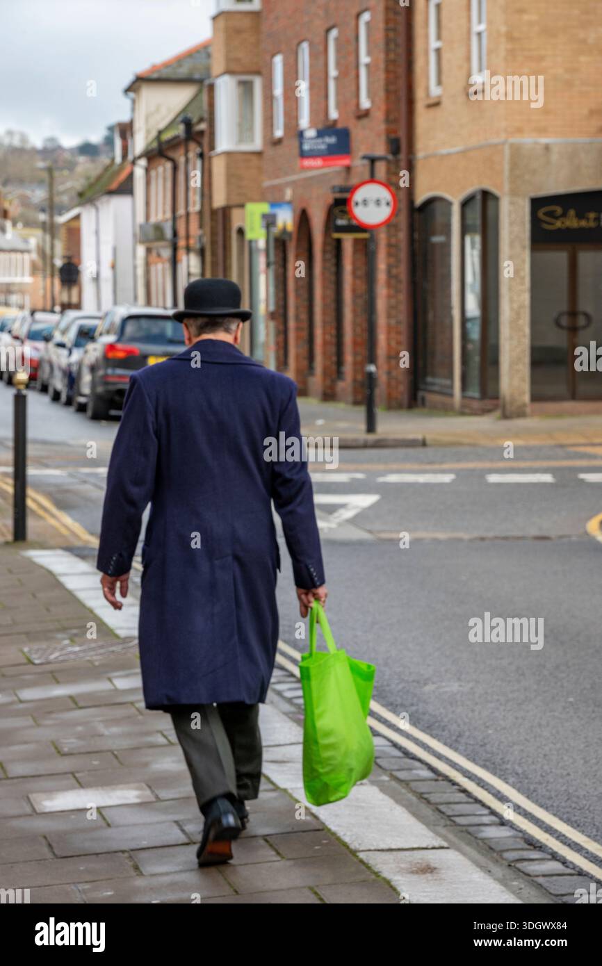 Habille intelligemment l'homme plus âgé portant chapeau Bowler et portant sac en plastique vert marchant seul le long d'une rue du centre-ville. Banque D'Images