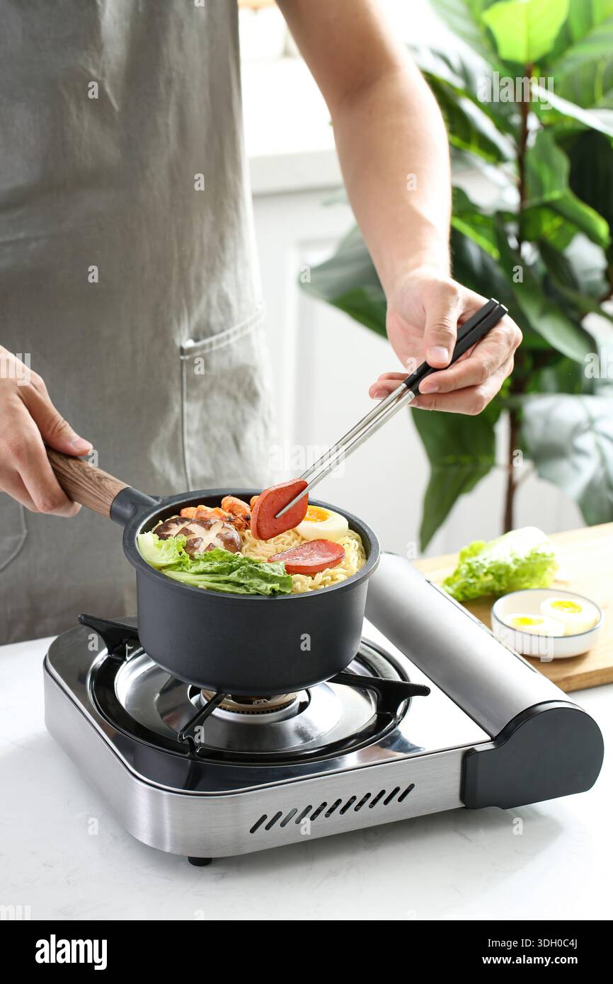 Personne cuisinant des nouilles instantanées avec des crevettes, des œufs et des légumes dans une petite casserole sur une cuisinière à gaz Banque D'Images