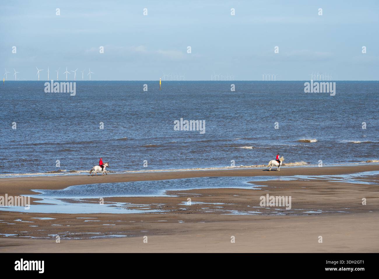 Les gens montent à cheval le long de Rossall Beach à Fleetwood, Lancashire, avec les parcs éoliens de la mer d'Irlande derrière. Banque D'Images