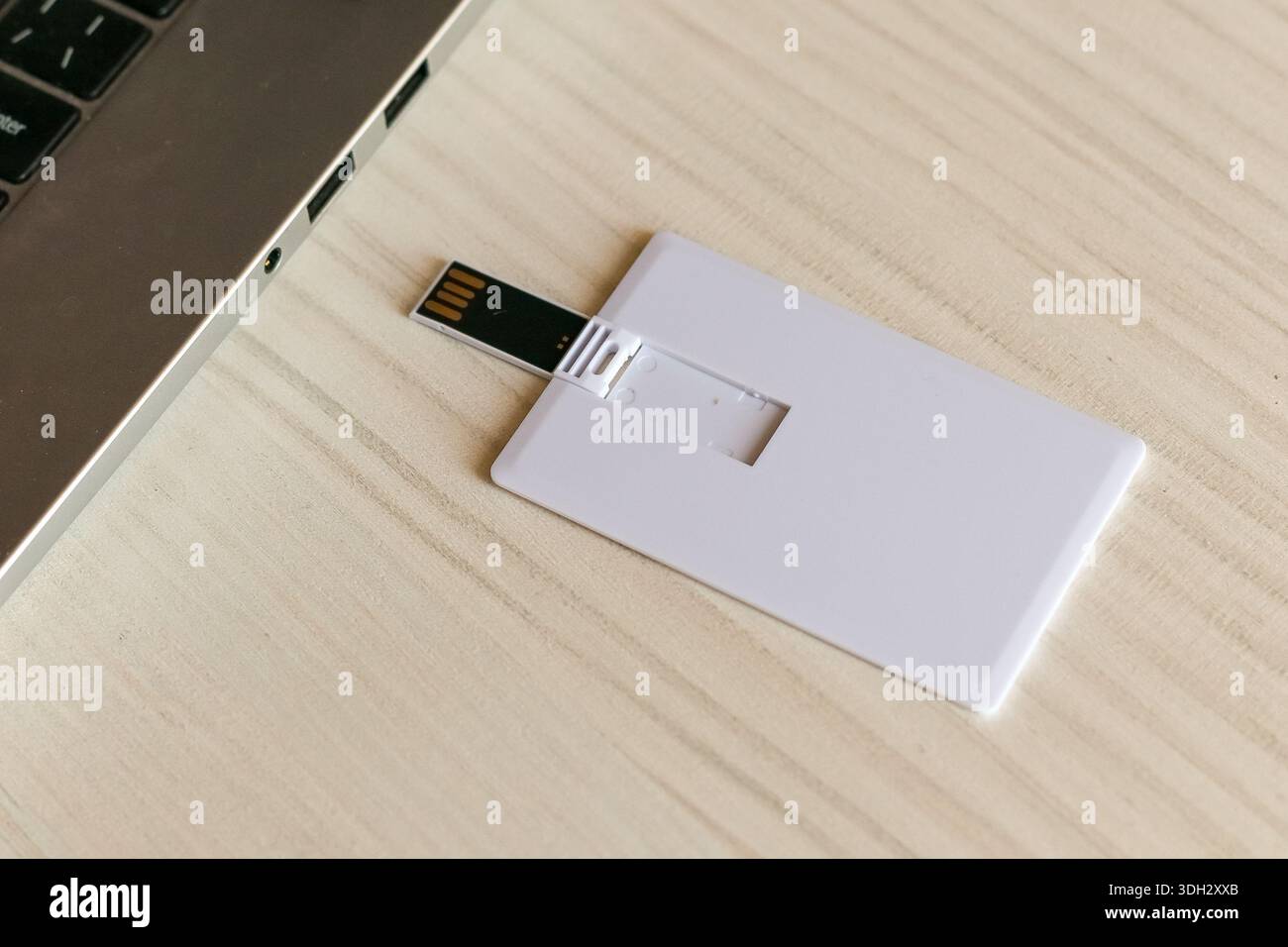 Clé USB mince en forme de carte de crédit avec clé flash étendue placée à côté d'un ordinateur portable argenté sur un bureau en bois, offrant un soluti de stockage de données mince Banque D'Images