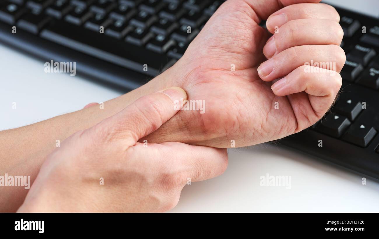 Un homme massant son poignet douloureux sur un fond de clavier d'ordinateur, illustrant l'inconfort du syndrome du canal carpien. Gros plan. Banque D'Images