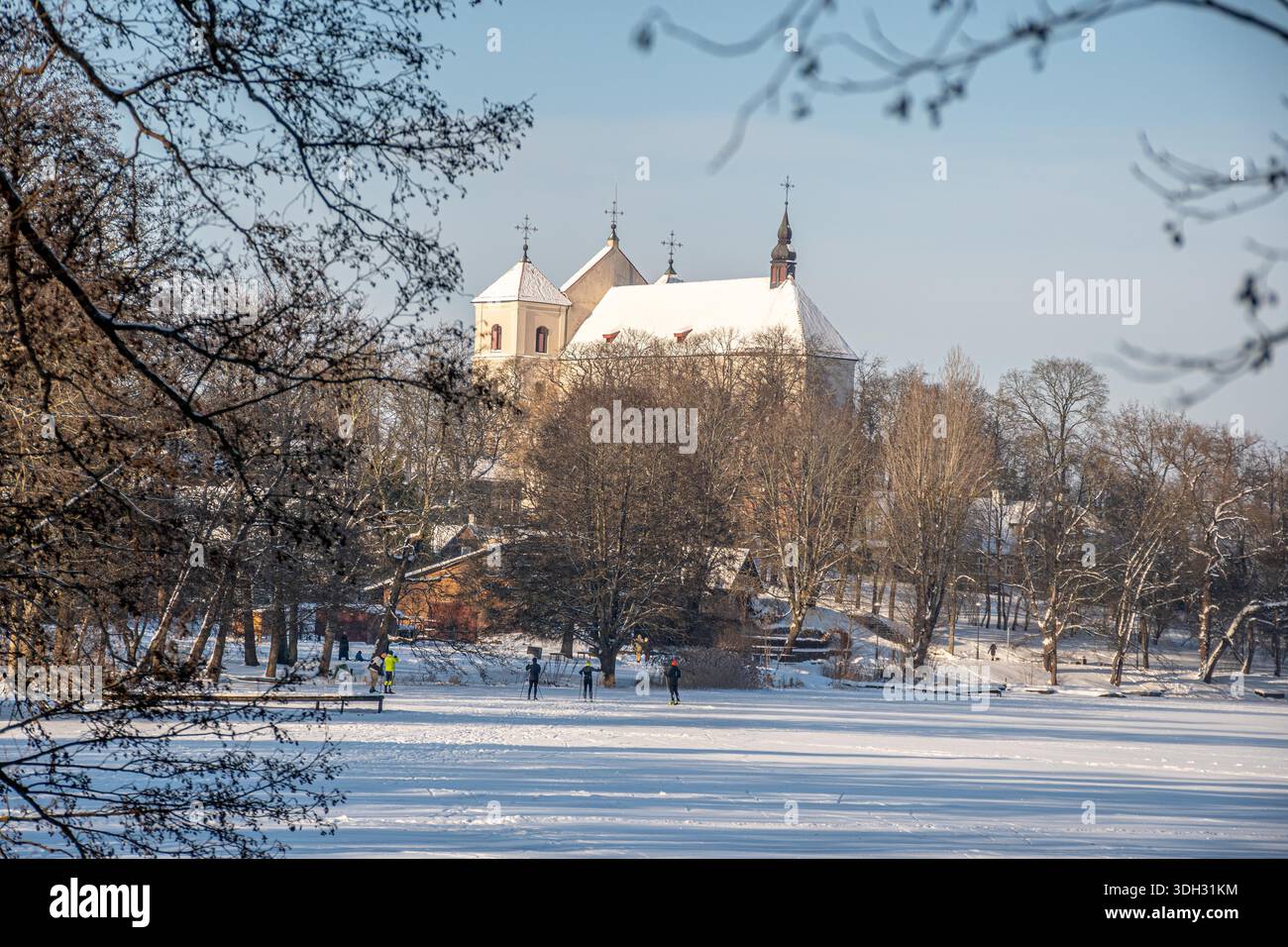Magnifique vue hivernale de Trakai, Vilnius, Lituanie, Europe du Nord, avec église et maisons couvertes par la neige et les gens skient sur le lac gelé Banque D'Images