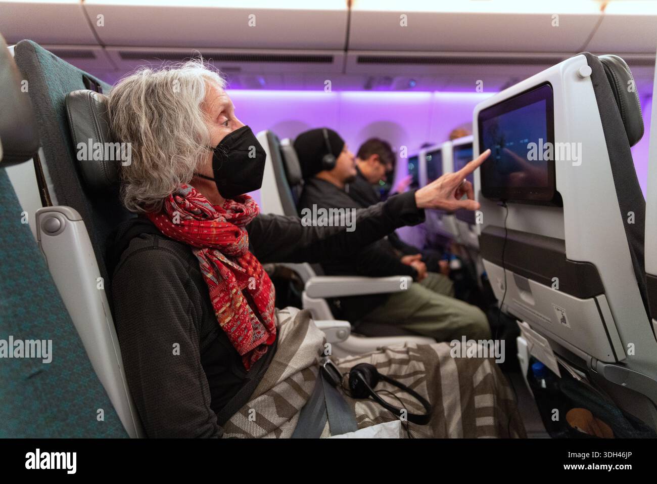 Le passager utilise l'écran de divertissement du dossier de siège lors d'un vol international sur une cabine d'avion moderne à large carrosserie. Banque D'Images
