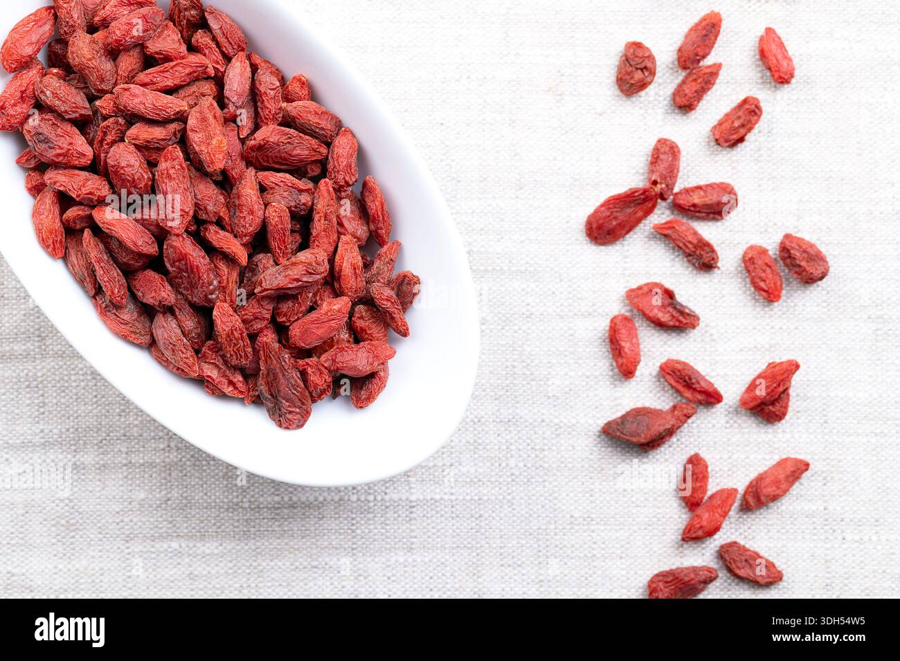 Baies de Goji, fruits secs dans un bol blanc sur lin. Aussi wolfberry chinois, médaillon rouge, et vigne matrimoniale. Fruits vifs, rouge orangé, sucrés. Banque D'Images