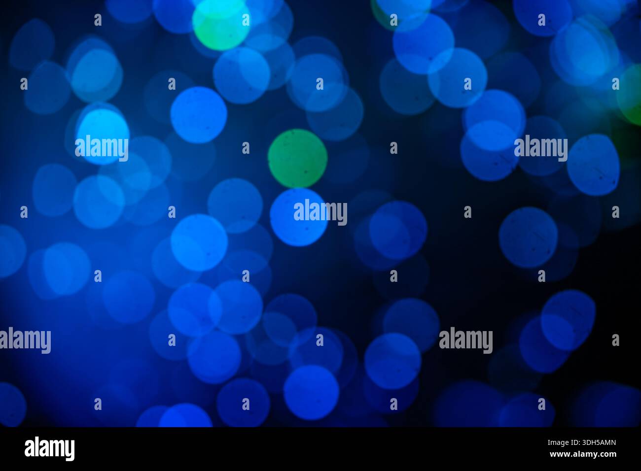 Une composition abstraite captivante avec des lumières bokeh bleues et vertes de différentes tailles. Les lumières créent un effet visuel époustouflant sur un dos sombre Banque D'Images
