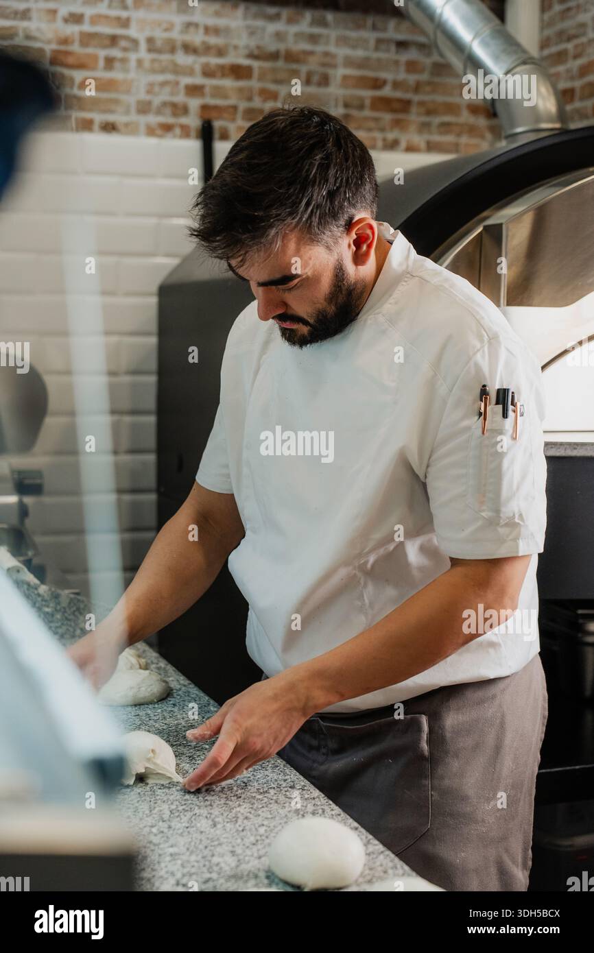 Un pizzeria qualifié fabrique de la pâte sur un comptoir en granit, vêtu d'une veste de chef blanche, entourée d'un décor rustique de briques et de TI Banque D'Images