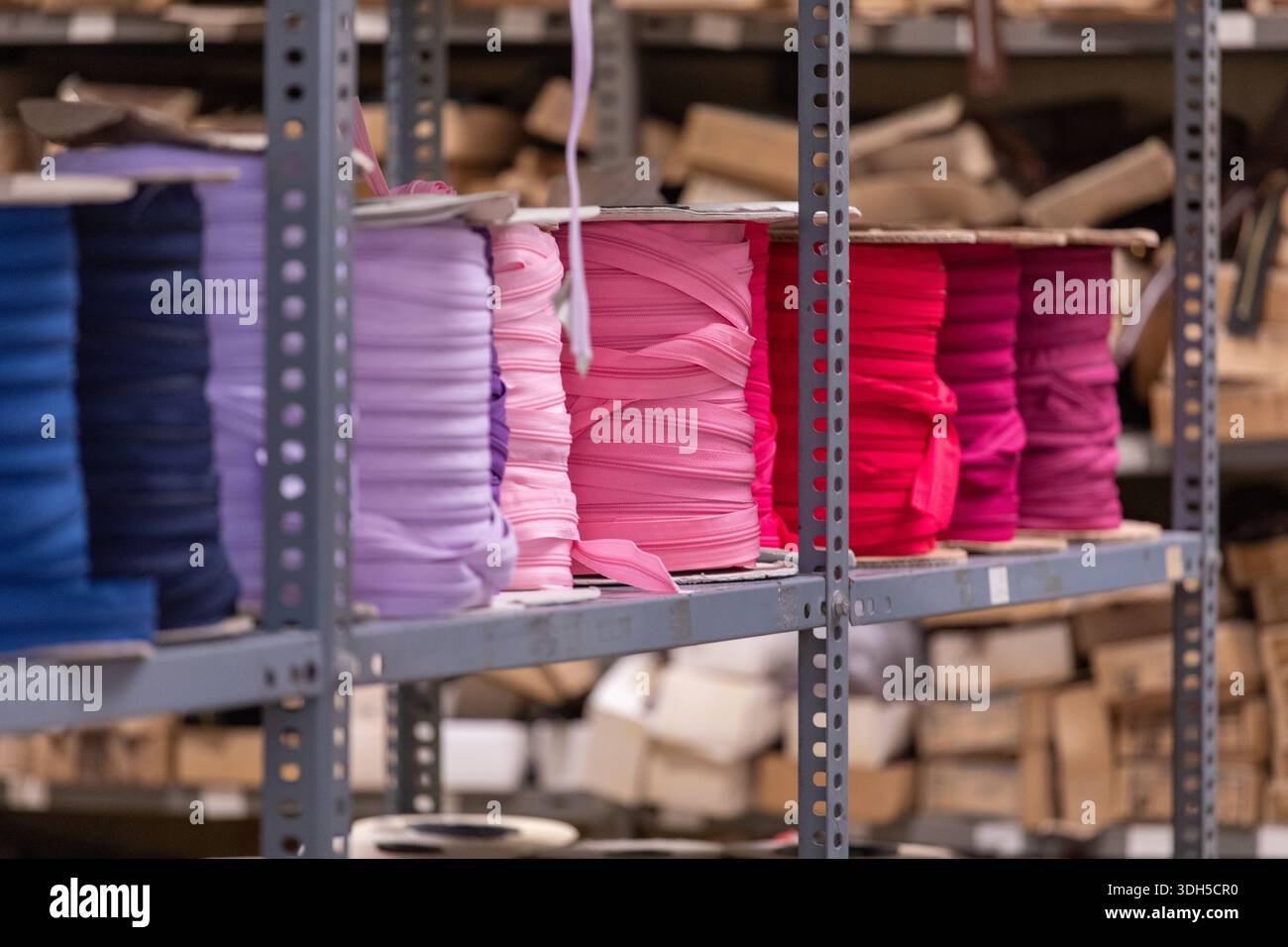 Des rouleaux de tissu empilés dans des tons vibrants de violet, rose et rouge sont soigneusement organisés sur des étagères en métal robustes dans un entrepôt, prêts à être utilisés dans divers Banque D'Images