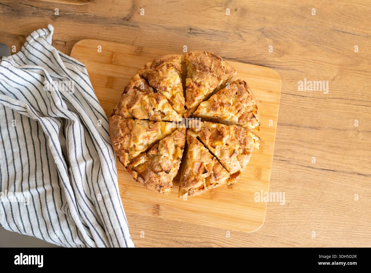 Une tarte aux pommes fraîchement cuite, coupée en huit morceaux, repose sur une planche à découper en bois. La croûte dorée et les morceaux de pomme visibles invitent à un réconfort, ho Banque D'Images