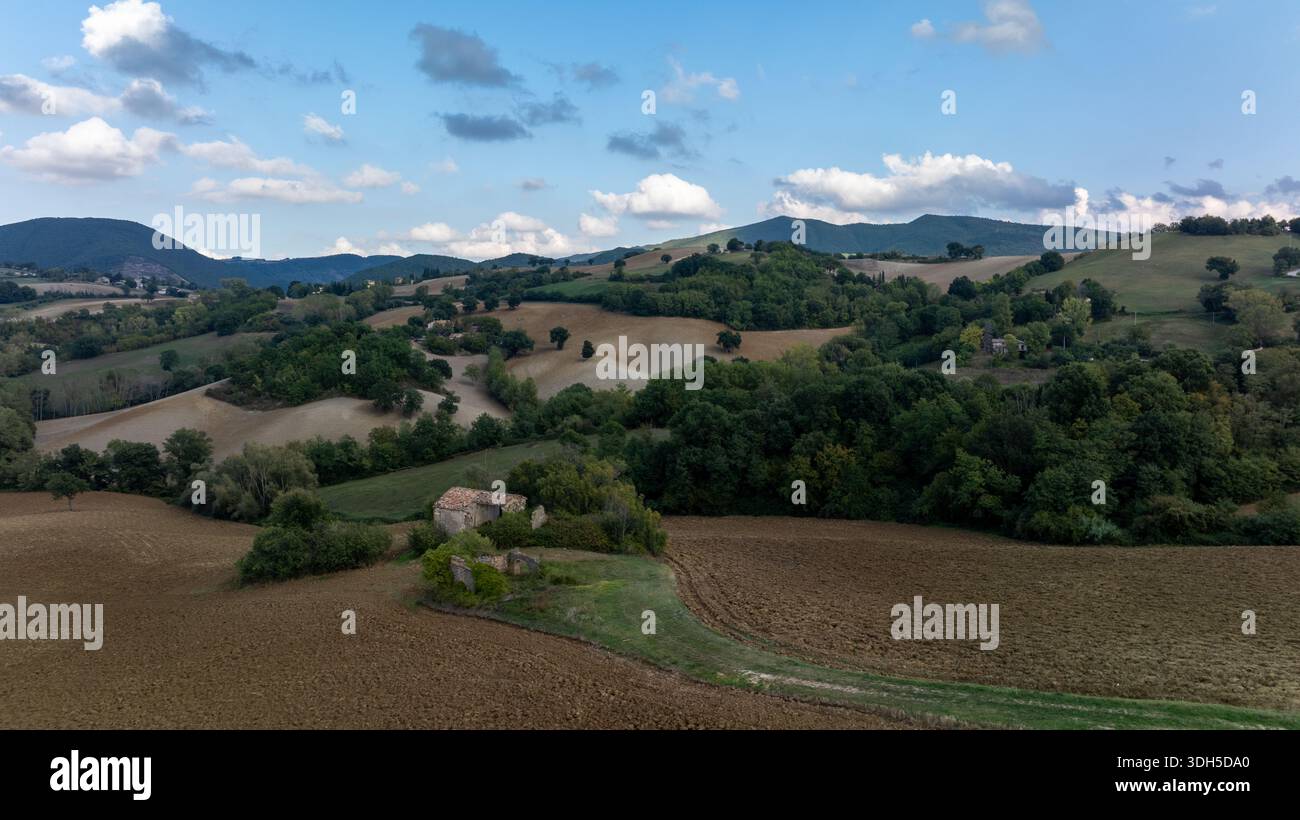Vue drone sur les collines ondoyantes de l'Italie, avec une végétation luxuriante, de vastes champs ouverts et des montagnes lointaines sous un ciel bleu serein, capturant l'esse Banque D'Images