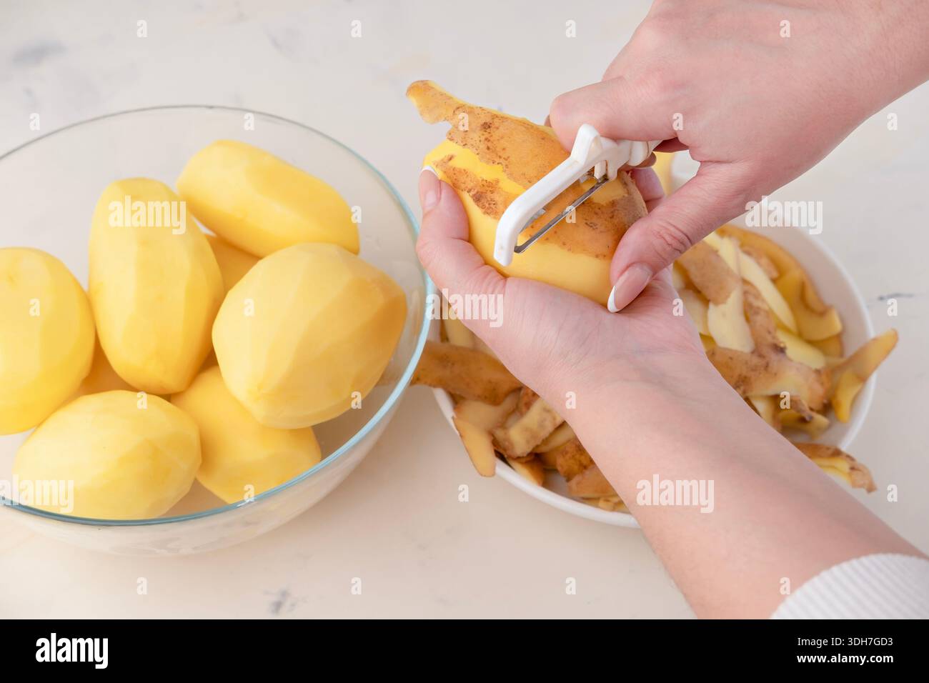 Mains d'une femme au foyer épluchant la pomme de terre crue avec un couteau d'outil spécial gros plan, vue de dessus. Banque D'Images